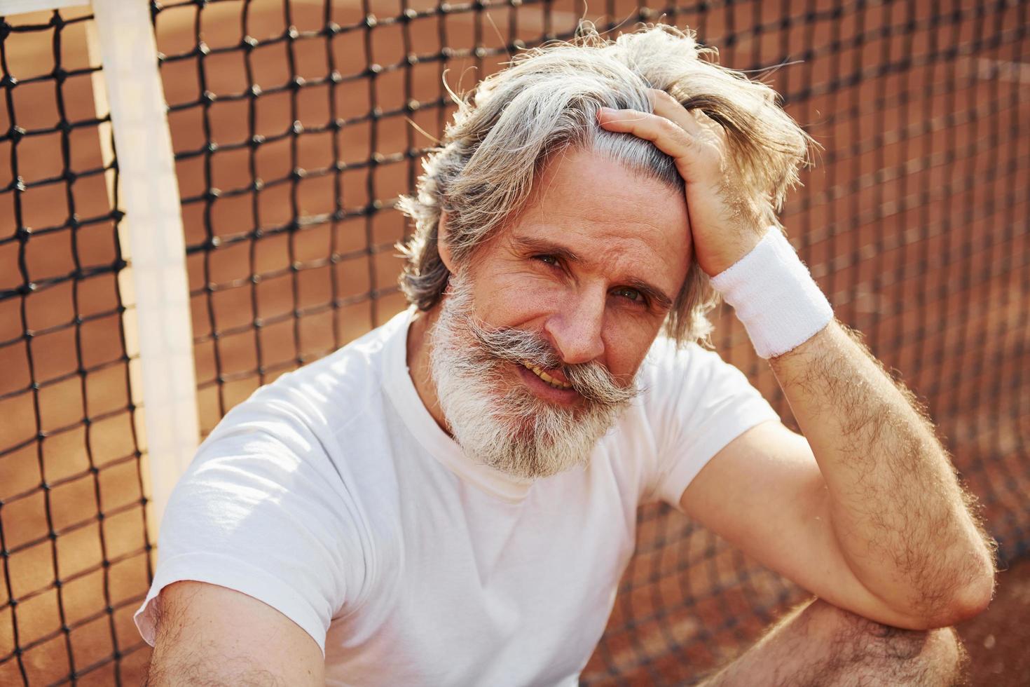 Älterer, moderner, stilvoller Mann mit Schläger im Freien auf dem Tennisplatz tagsüber foto