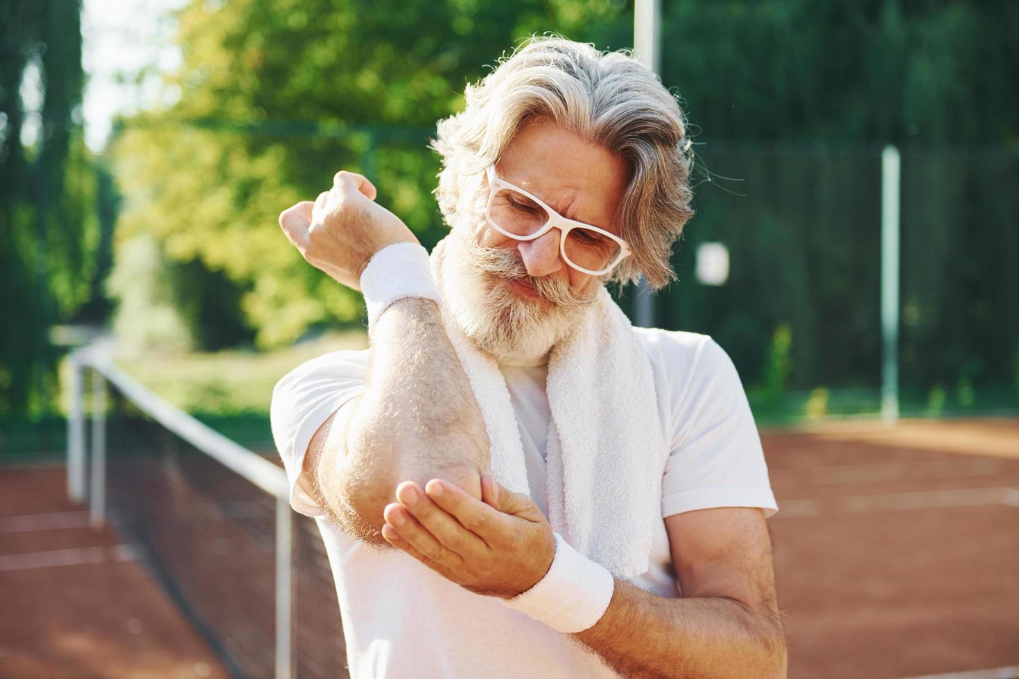 Schmerzgefühl aufgrund eines Traumas. Älterer, moderner, stilvoller Mann im Freien auf dem sportlichen Feld tagsüber foto