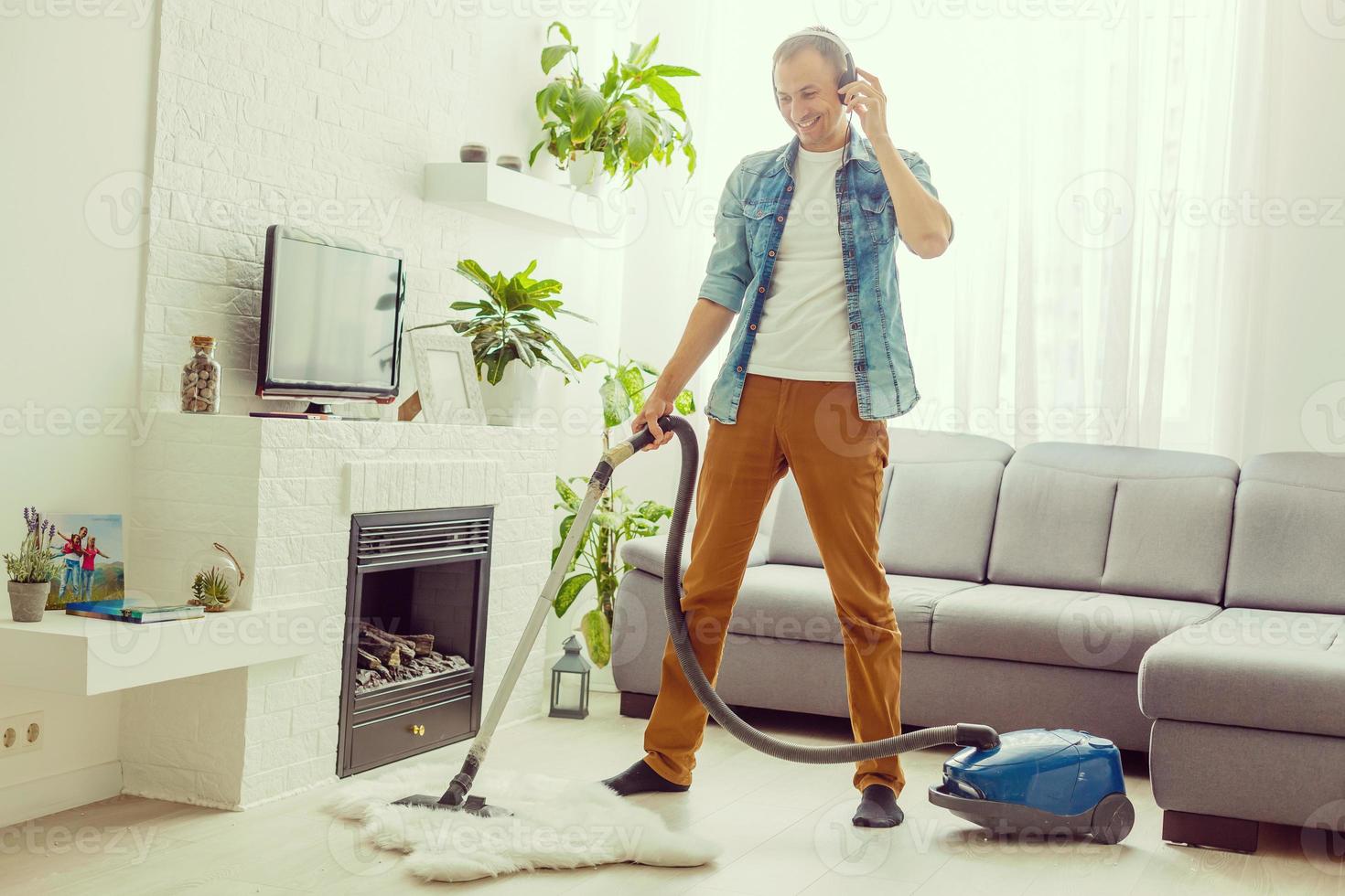 junger mann, der spaß hat, haus mit staubsauger zu putzen, der wie gitarrist tanzt foto