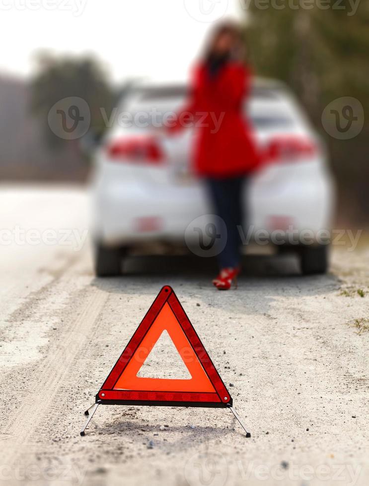 Frau, die neben dem kaputten Auto und dem Warndreieck steht foto