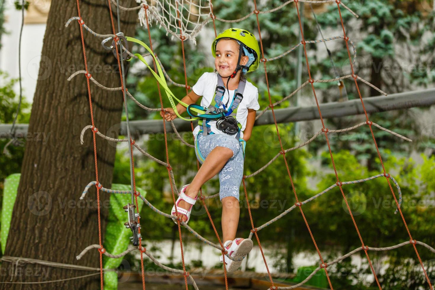 glückliches Schulmädchen, das Aktivität in einem Kletterabenteuerpark an einem Sommertag genießt foto