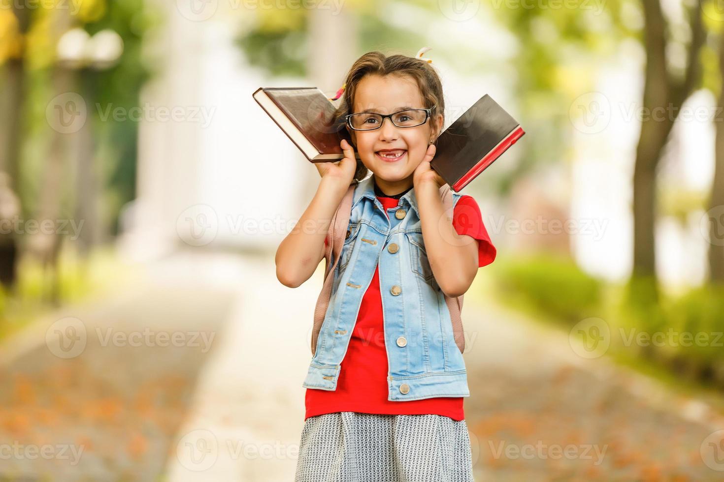 porträt eines attraktiven kaukasischen kleinen studentenmädchens mit schönen braunen augen. glückliches lächelndes kind, das kamera betrachtet - nahaufnahme, draußen. foto