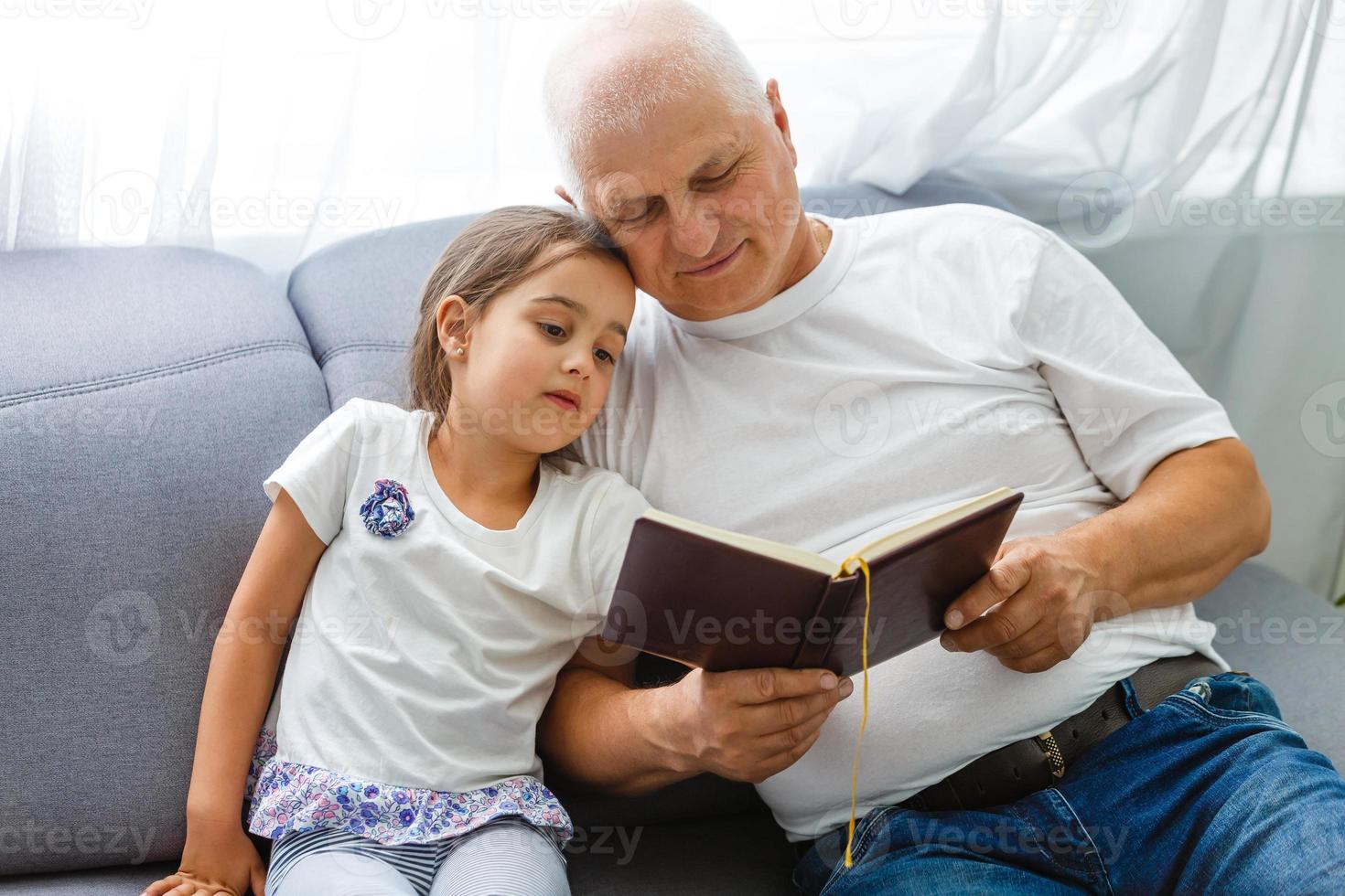 glückliches kleines mädchen mit großvater, der zu hause ein geschichtenbuch liest foto