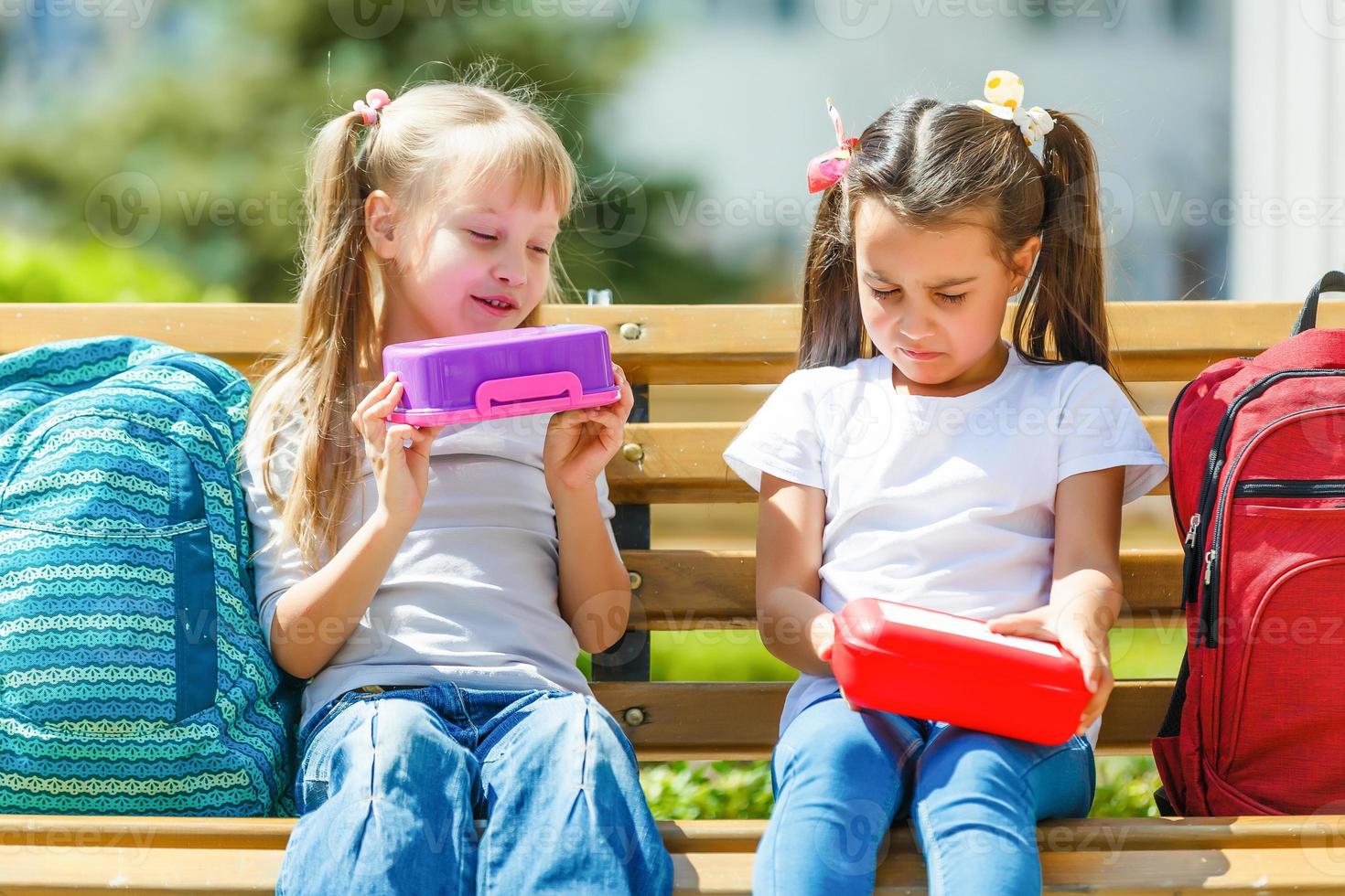 Grundschulkinder sitzen mit Lunchpaketen foto