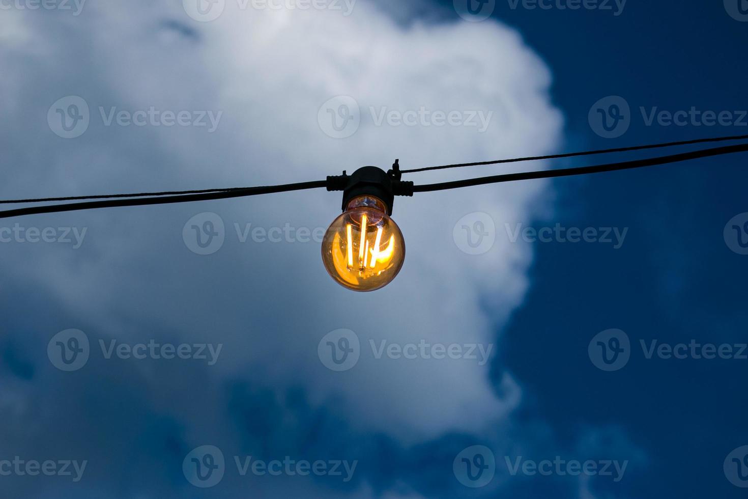 Nahaufnahme eines Glühfadens im Edison-Stil auf einer Glühbirne vor einem bewölkten Himmel. Energiekrise. foto
