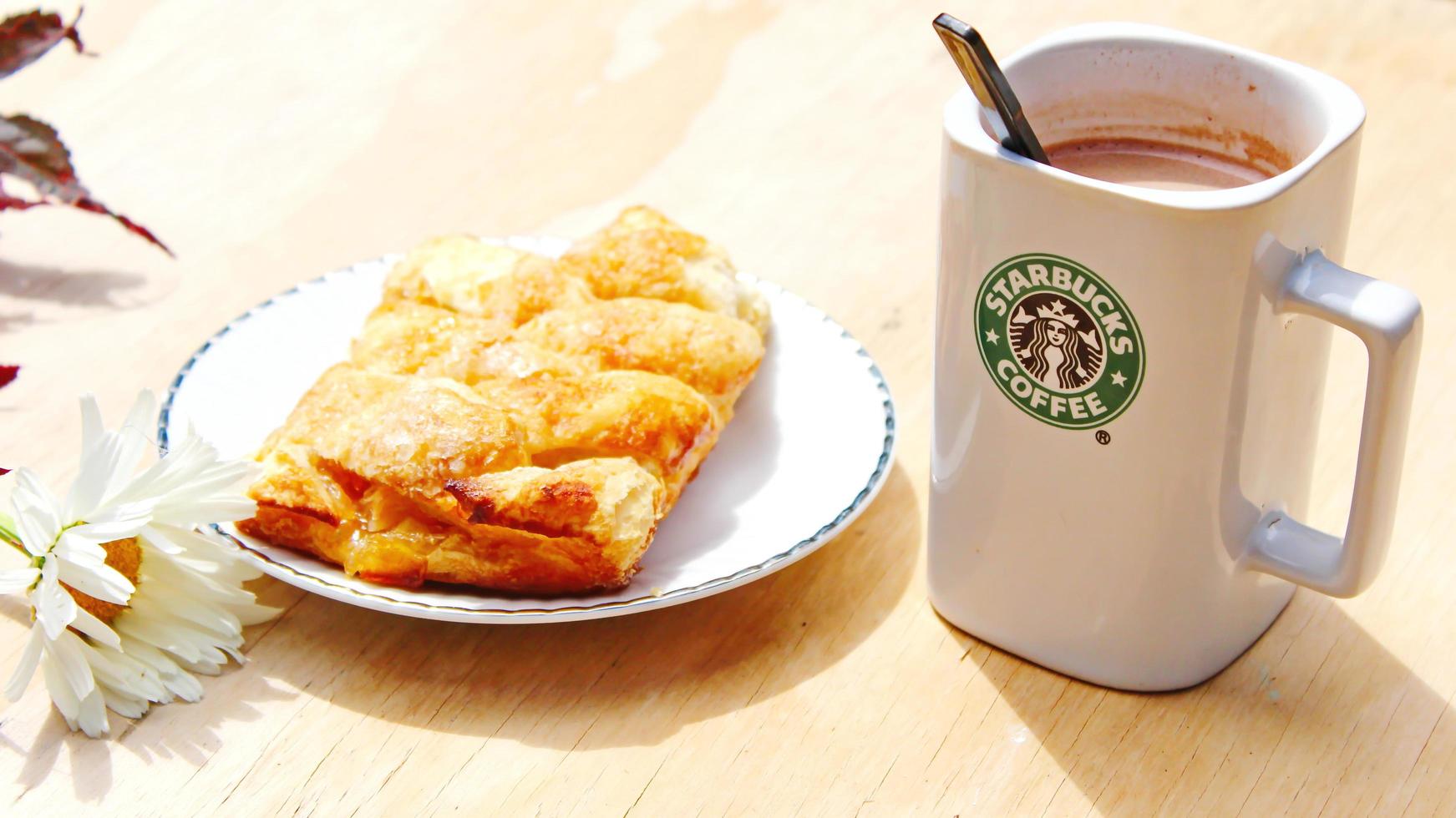 washington, usa - 01. august 2022 kaffeebecher mit starbucks-logo auf der vorderseite, weiße bäckerei auf dem teller. Stellen Sie es auf einen Holztisch im Garten, wo die Morgensonne scheint. foto