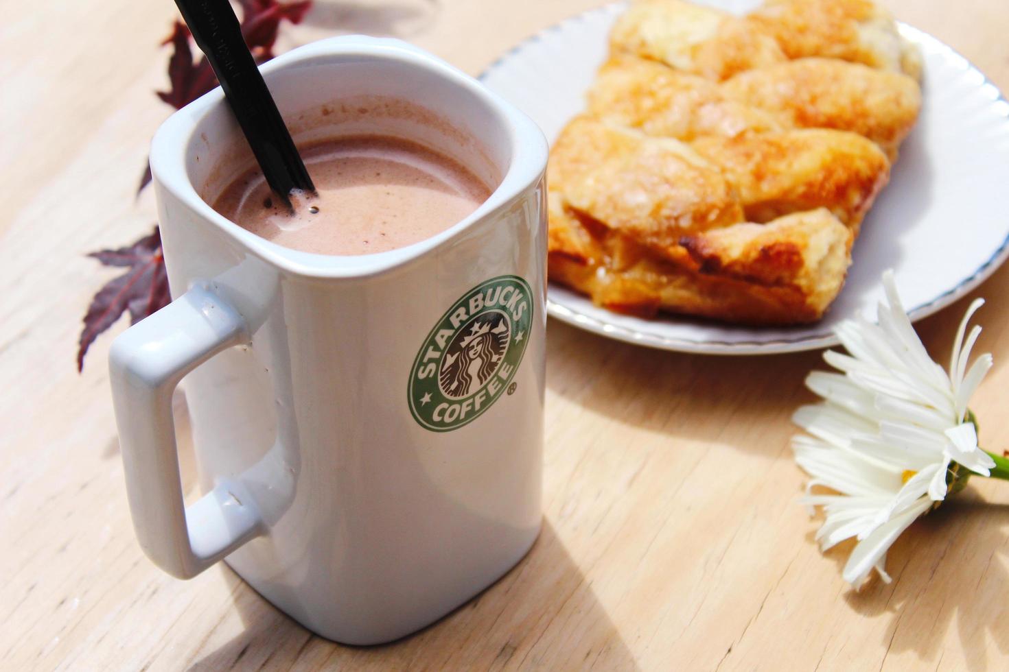 washington, usa - 01. august 2022 kaffeebecher mit starbucks-logo auf der vorderseite, weiße bäckerei auf dem teller. Stellen Sie es auf einen Holztisch im Garten, wo die Morgensonne scheint. foto