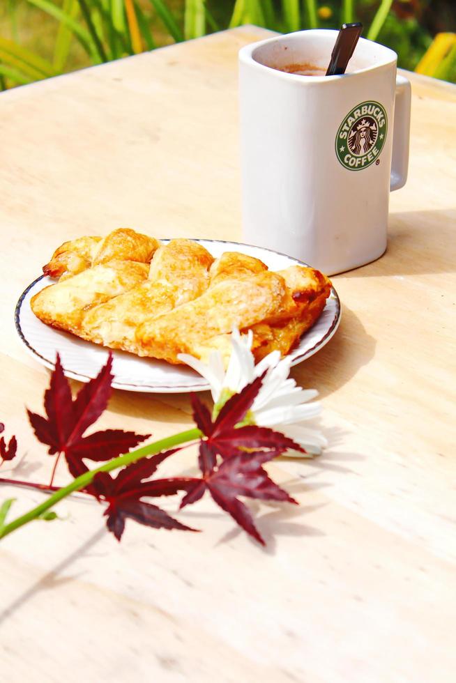 washington, usa - 01. august 2022 kaffeebecher mit starbucks-logo auf der vorderseite, weiße bäckerei auf dem teller. Stellen Sie es auf einen Holztisch im Garten, wo die Morgensonne scheint. foto