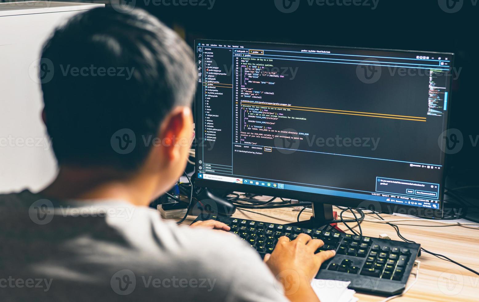 Rückansicht Junger asiatischer Mann, der am Schreibtisch sitzt und Computerprogrammierungs-Debugging verwendet, um den Code des binären Algorithmus in der Workstation zu verbessern, indem er sich auf den Monitor konzentriert und Menschen verwischt foto