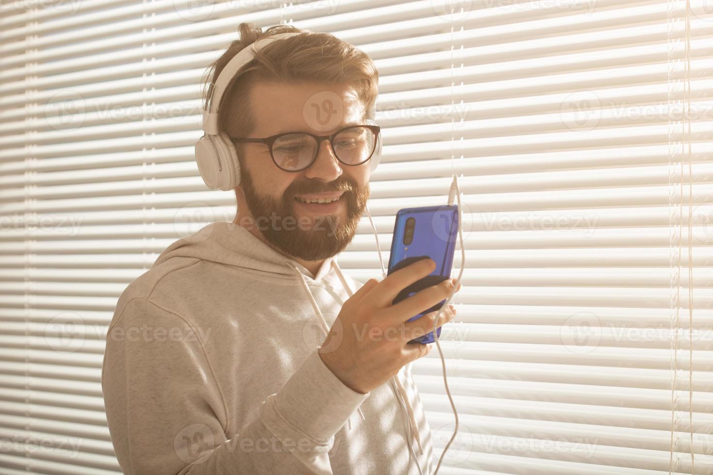 nahaufnahmeporträt eines jungen, stilvollen hipster-mannes, der lieblingsmusik auf dem smartphone mit kopfhörern im büro auswählt. musikabonnementkonzept foto