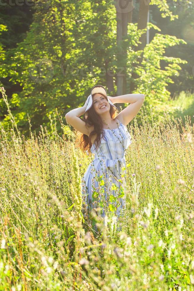 junge Frau, die an einem sonnigen Sommertag zwischen Wildblumen spazieren geht. Konzept der Freude an der Kommunikation mit der Sommernatur foto