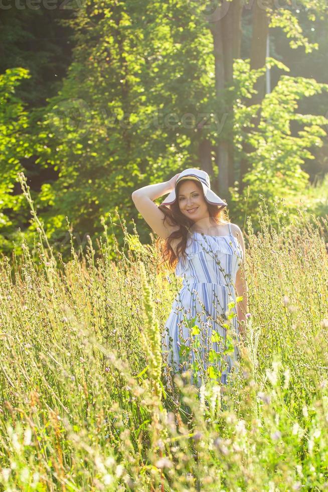 junge Frau, die an einem sonnigen Sommertag zwischen Wildblumen spazieren geht. Konzept der Freude an der Kommunikation mit der Sommernatur foto