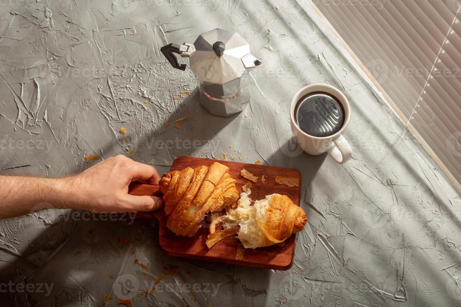 frühstück mit croissant auf schneidebrett und schwarzem kaffee. Morgenmahlzeit und Frühstückskonzept. foto