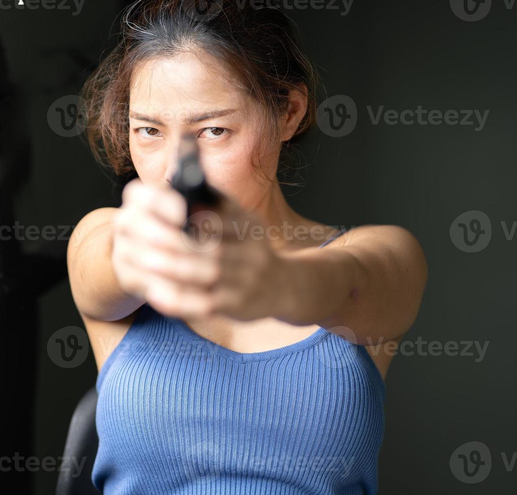 junge frau mit pistole, die auf eine gefährliche kriminalitätsperson abzielt. schöne asiatische spionageagentin, die pistolenwaffe zeigt, um gangster zu verteidigen, porträt. frau, die ein waffen-selbstschutzkonzept schießt foto