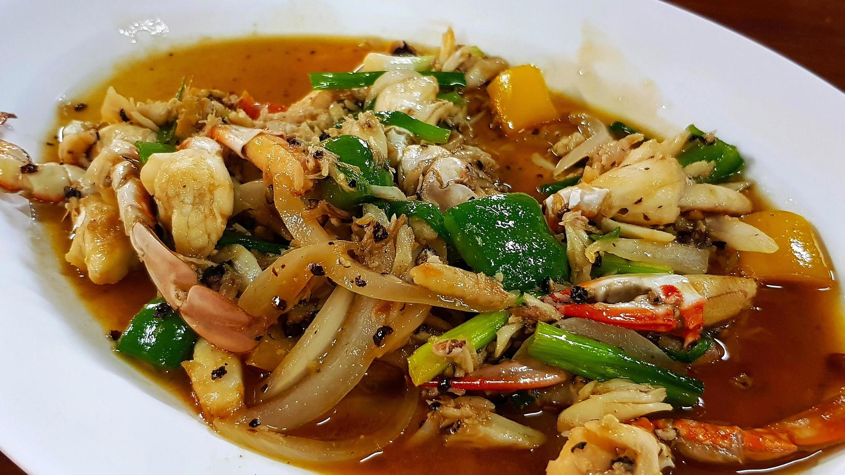 Gebratene Krabben mit schwarzem Pfeffer, geschnittenen Zwiebeln, Paprika und Frühlingszwiebeln auf weißem Teller oder Teller im thailändischen Restaurant umrühren. asiatisches und berühmtes essen mit meeresfrüchten in thailand. foto