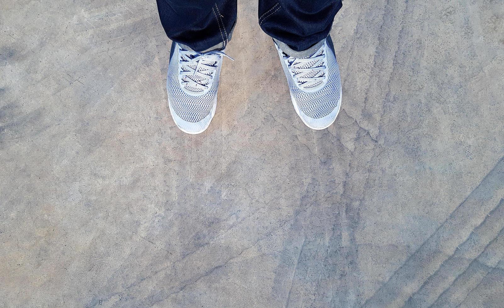 Blick von oben auf das Bein mit blauen Jeans und grauen oder grauen Turnschuhen oder modischen Schuhen auf dem Boden mit Autorad oder Bremsspur auf der Straße oder Straße mit Kopierraum. flache Lage des Teilkörpers. abstrakter Hintergrund foto