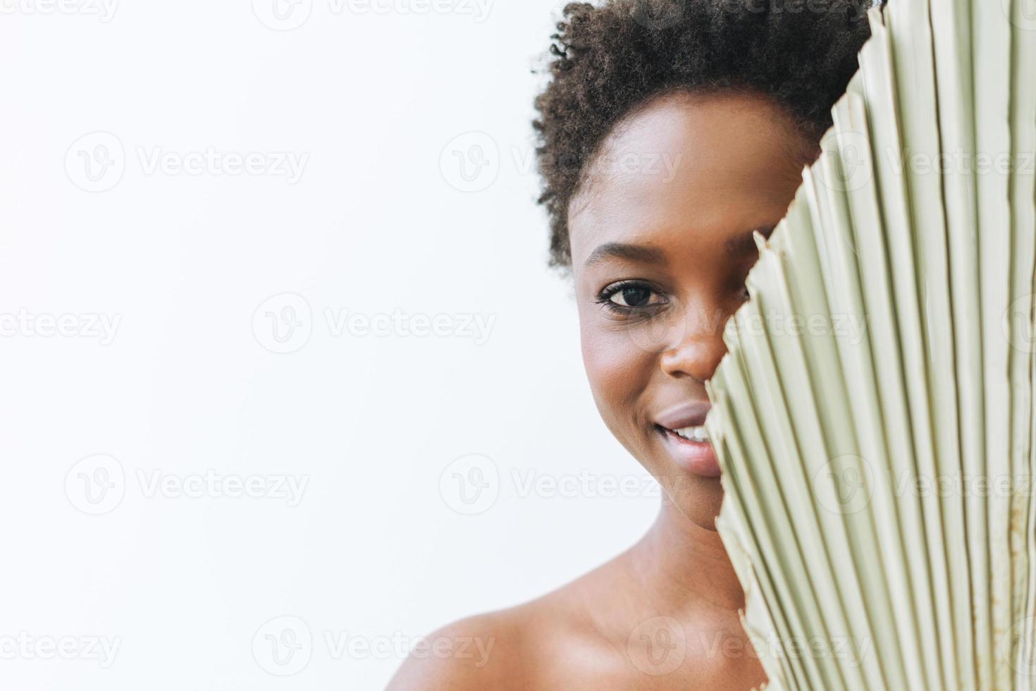 schönes lächelndes afroamerikanisches Schönheitsmodemodell der jungen Frau, das Kamera mit trockenem Blatt auf weißem Hintergrund, Ökokonzept, Naturschönheit betrachtet foto