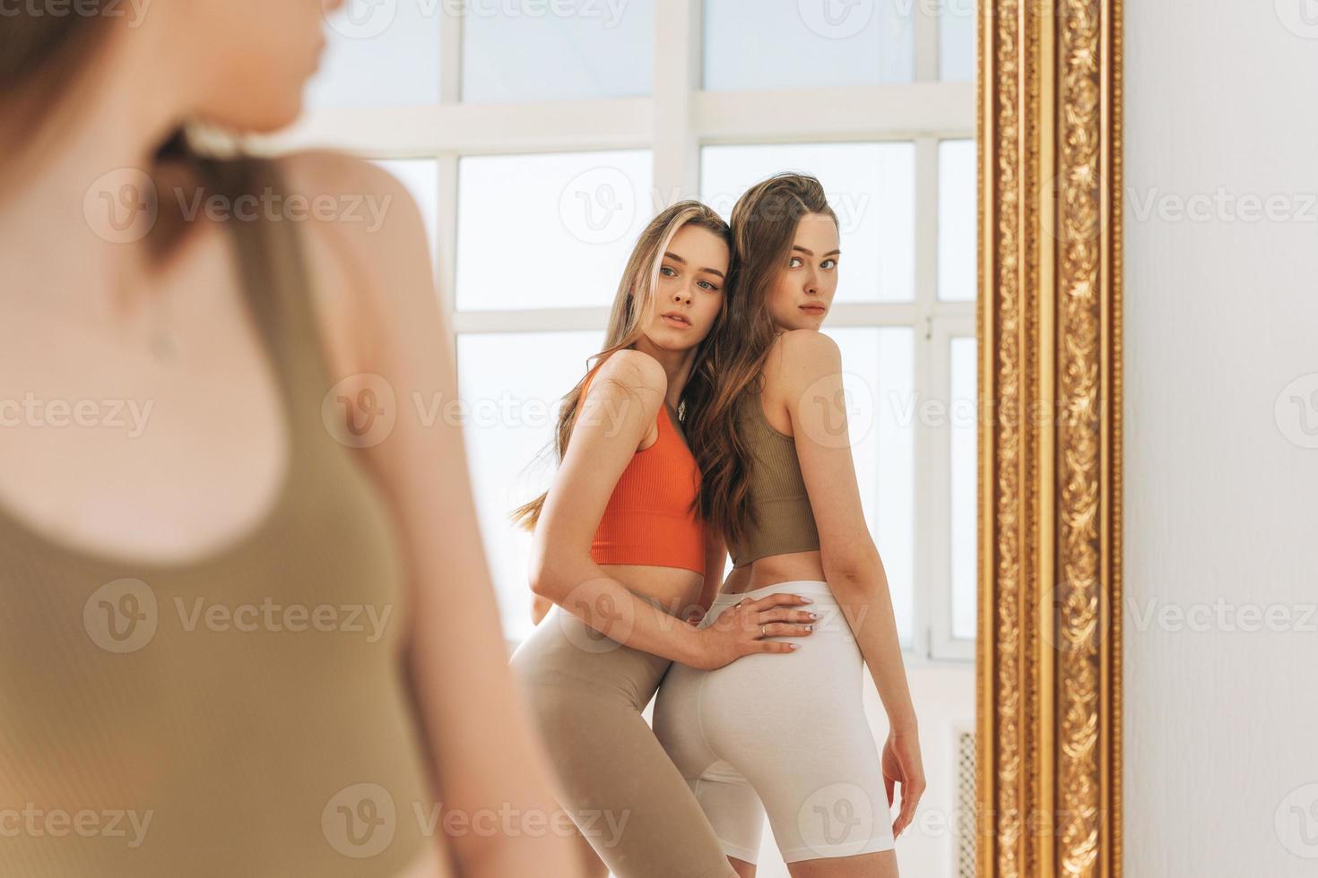 Fashion Beauty Models Zwei Schwestern zwillinge schöne Mädchen mit langen Haaren in Sportbekleidung, die im hellen Studio spiegeln foto