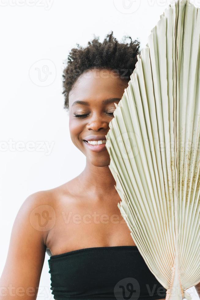 Schöne lächelnde afroamerikanische junge Frau mit engen Augen Schönheitsmodemodell mit trockenem Blatt auf weißem Hintergrund, Ökokonzept foto