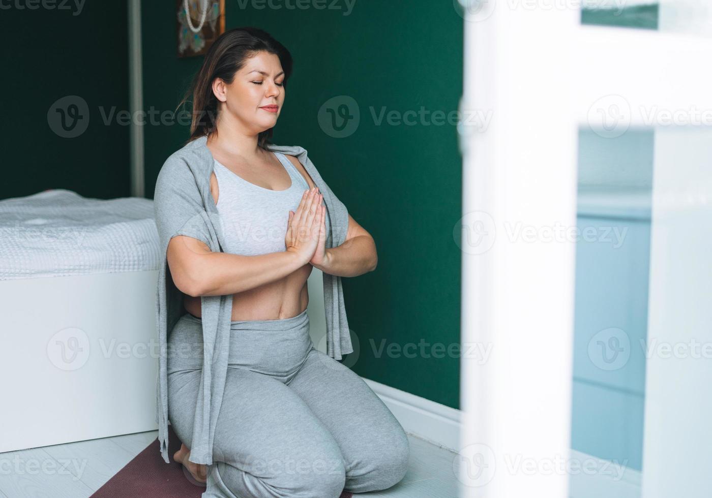 schöne brünette junge frau plus größenkörper positiv in bequemer sportkleidung praktiziert yoga online zu hause foto