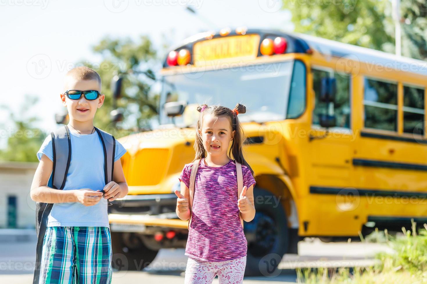 Schönes kleines Schulmädchen mit Klassenkameraden in der Nähe des Schulbusses foto