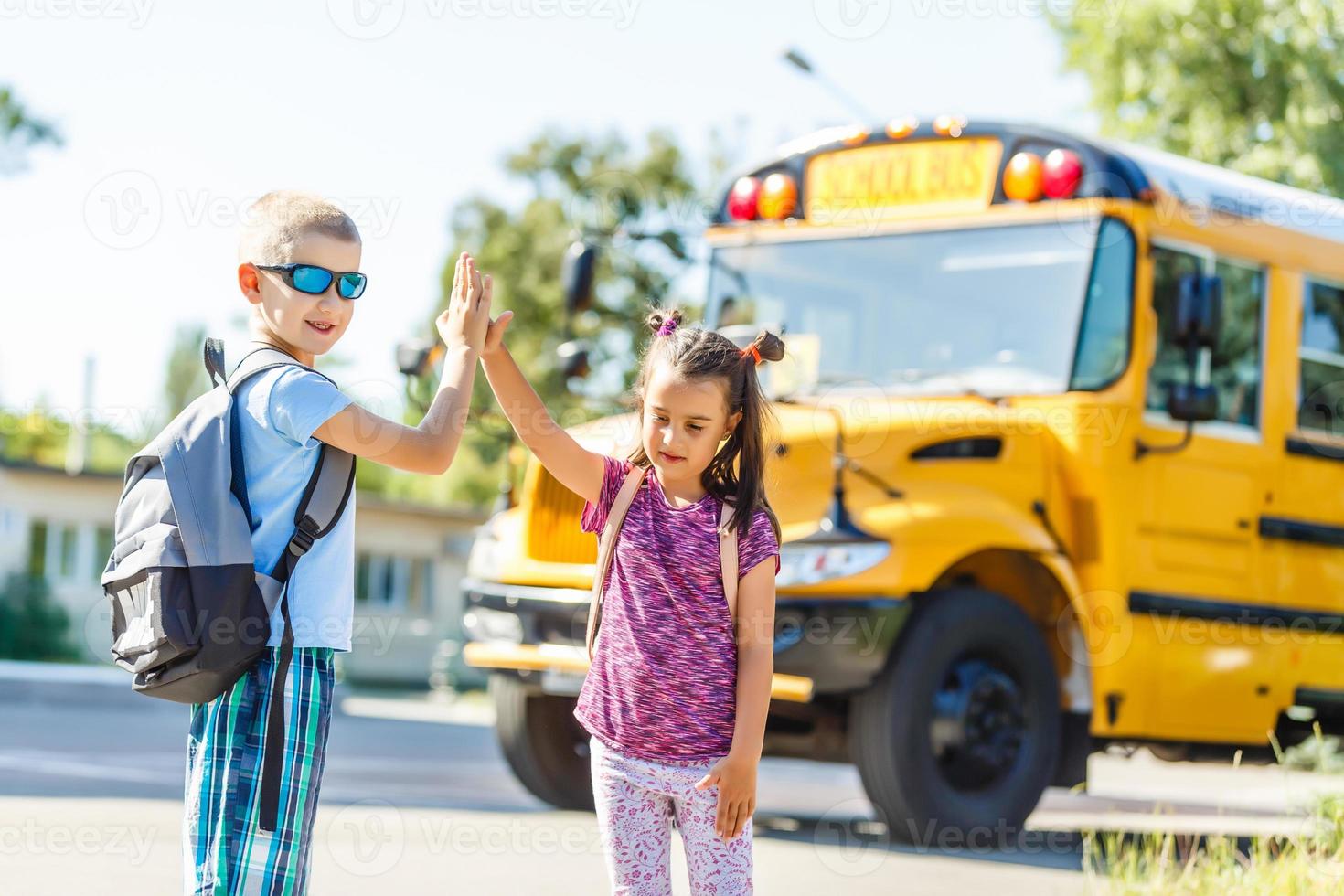 Schönes kleines Schulmädchen mit Klassenkameraden in der Nähe des Schulbusses foto