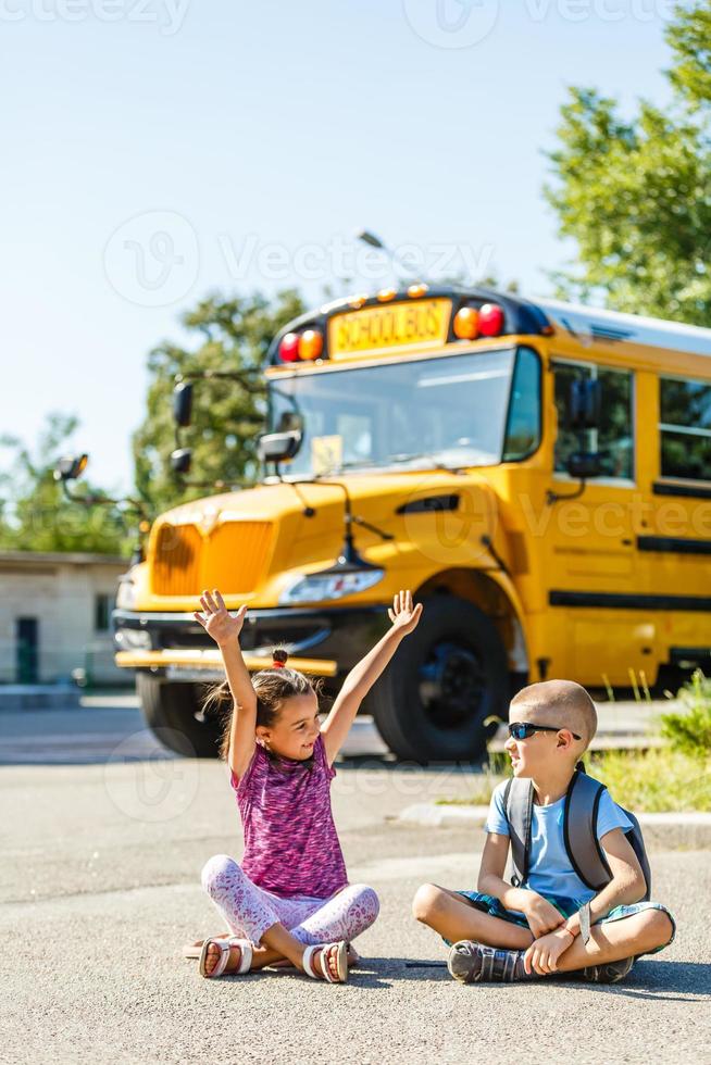 Schönes kleines Schulmädchen mit Klassenkameraden in der Nähe des Schulbusses foto