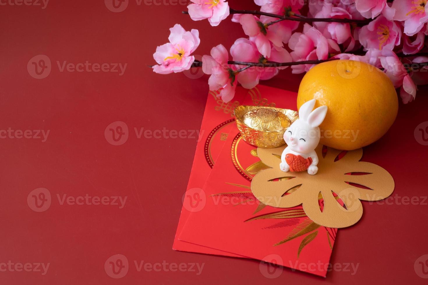 chinesisches neujahr des kaninchenfestivalkonzepts. Mandarinorange, rote Umschläge, Kaninchen und Goldbarren, verziert mit Pflaumenblüte auf rotem Hintergrund. foto