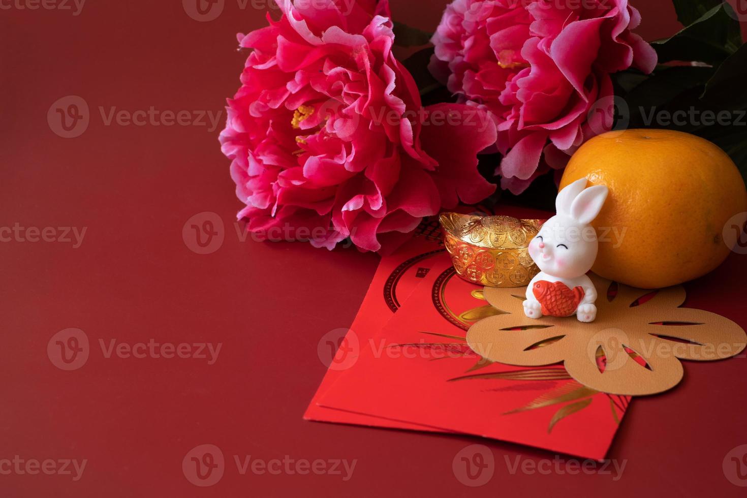 chinesisches neujahr des kaninchenfestivalkonzepts. Mandarinorange, rote Umschläge, Kaninchen und Goldbarren, verziert mit Pflaumenblüte auf rotem Hintergrund. foto