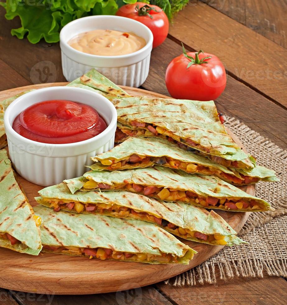 mexikanische Quesadilla in Scheiben geschnitten mit Gemüse und Saucen auf dem Tisch foto