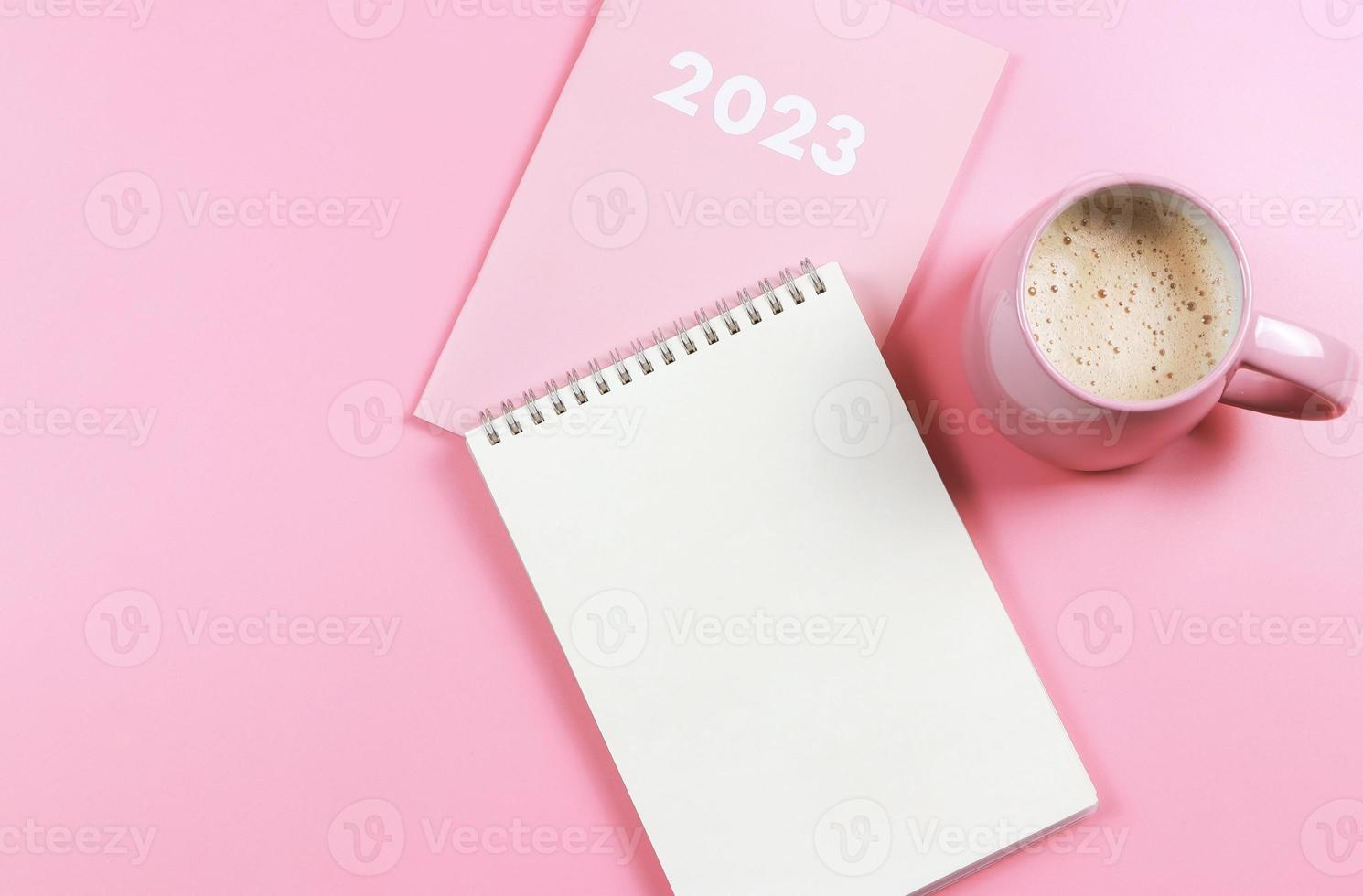 Flaches Notizbuch aus leerem Papier auf rosafarbenem Tagebuch 2023 und rosafarbener Tasse Kaffee auf rosafarbenem Hintergrund. foto
