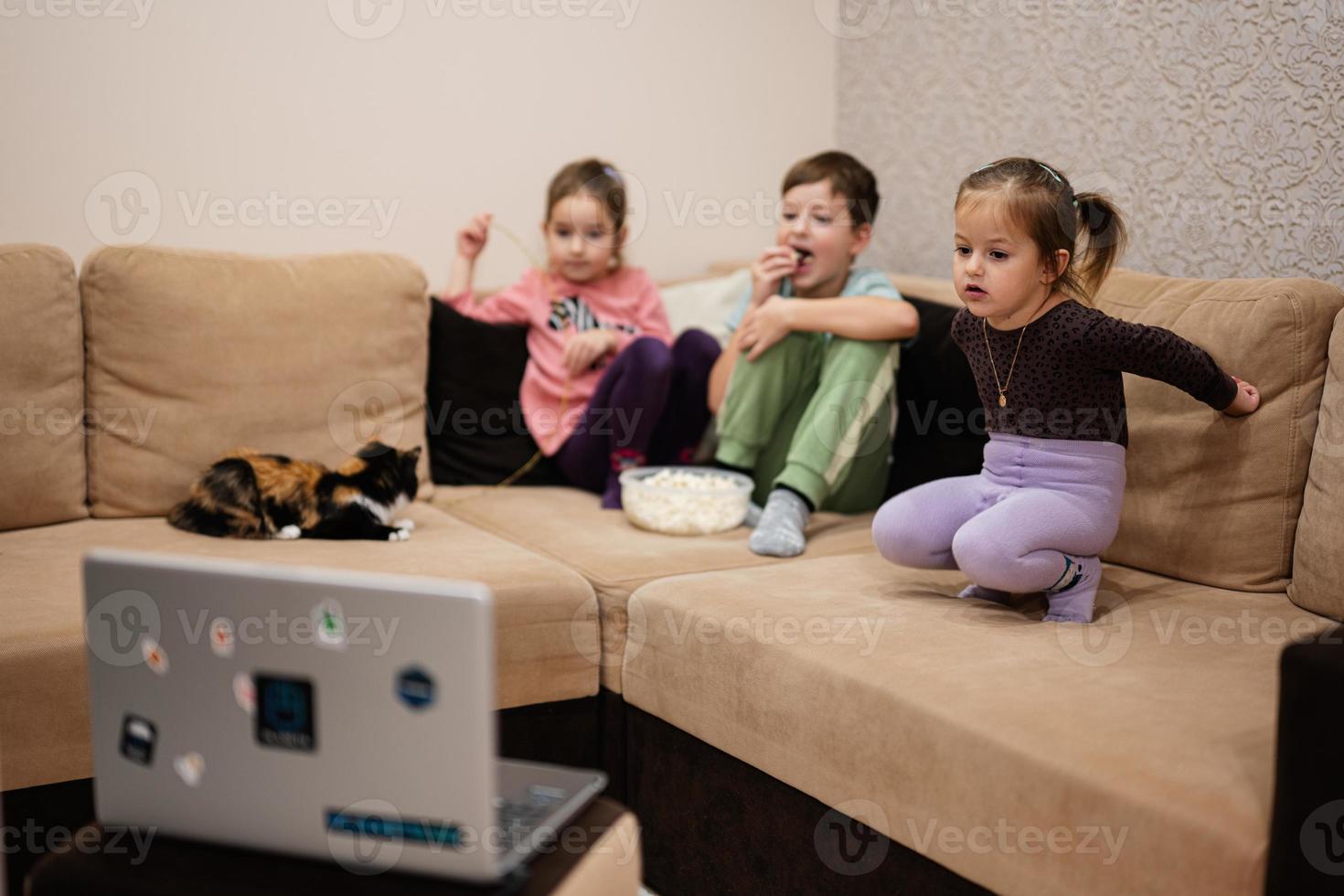 drei kinder mit kätzchen sitzen im wohnzimmer und schauen sich filme oder cartoons vom laptop an. foto