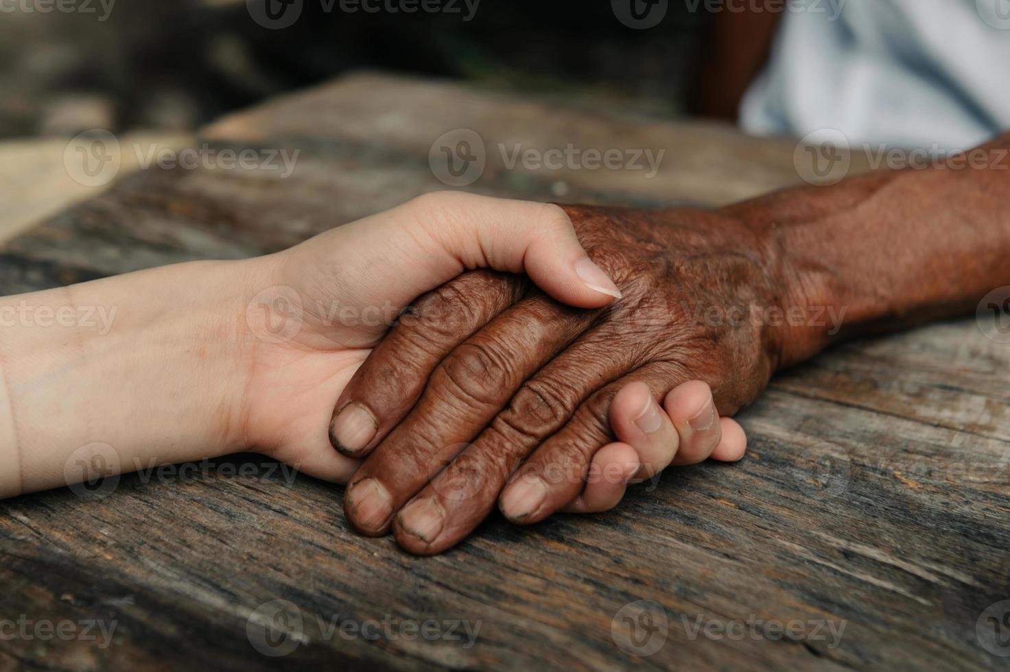 hände des alten mannes und einer frauenhand auf dem holztisch im sonnenlicht foto