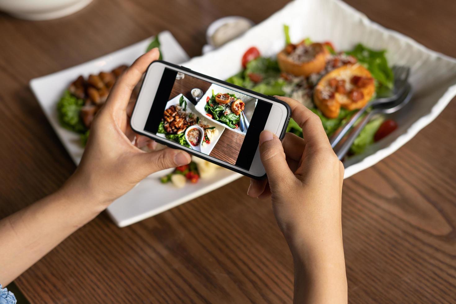 Frau fotografiert eine Mahlzeit auf dem Tisch, nachdem sie online Essen bestellt hat, um es zu Hause zu essen. fotografieren und telefonkonzepte verwenden foto