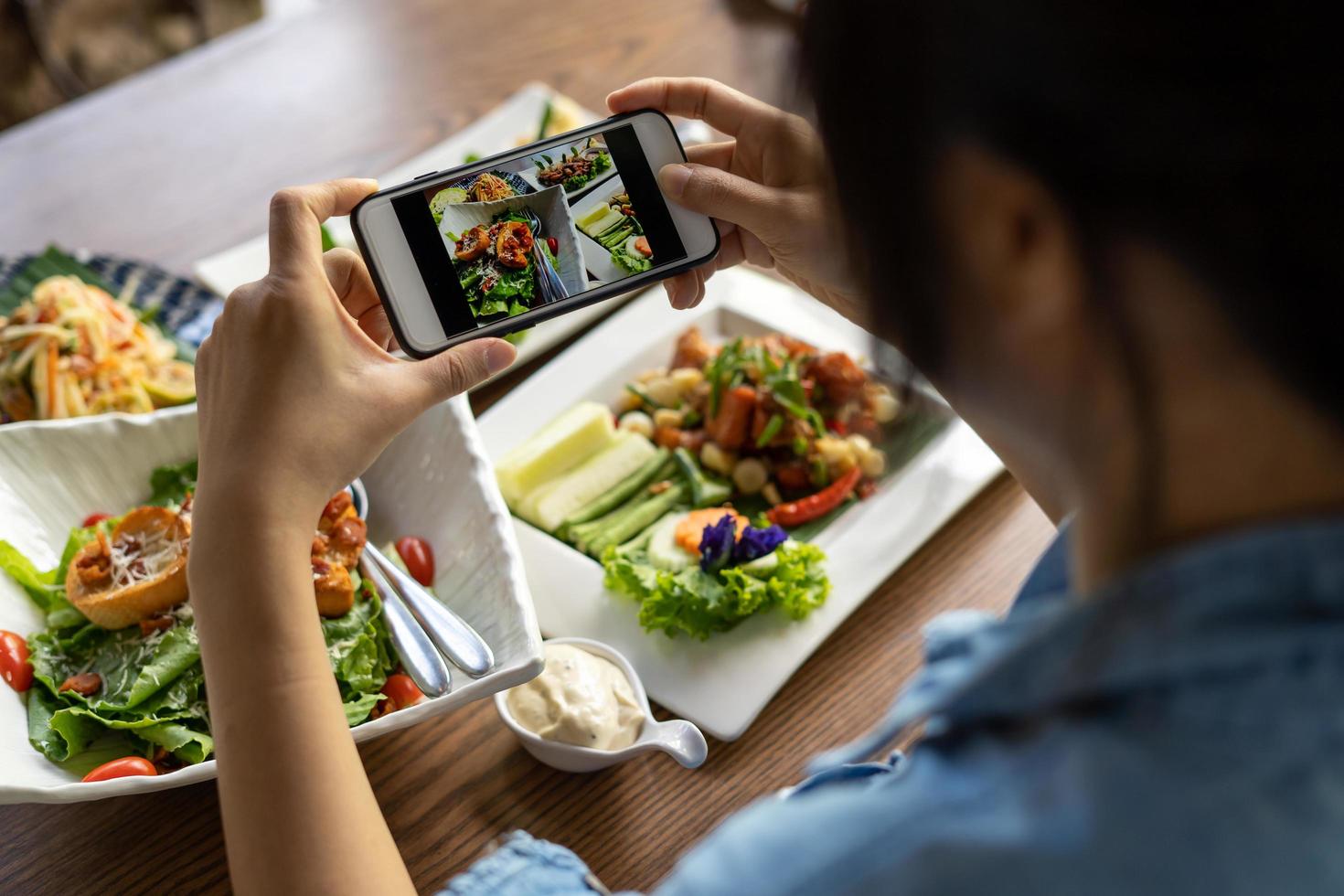 Frau fotografiert eine Mahlzeit auf dem Tisch, nachdem sie online Essen bestellt hat, um es zu Hause zu essen. fotografieren und telefonkonzepte verwenden foto