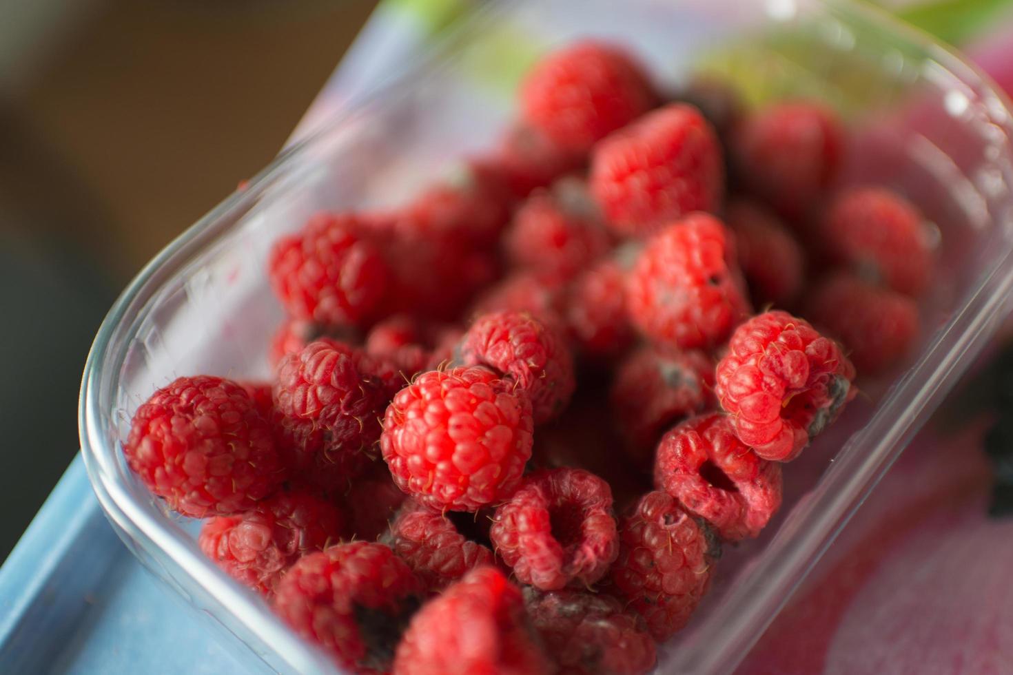 Nahaufnahme eines Plastikbehälters mit Himbeeren in schlechtem Zustand foto