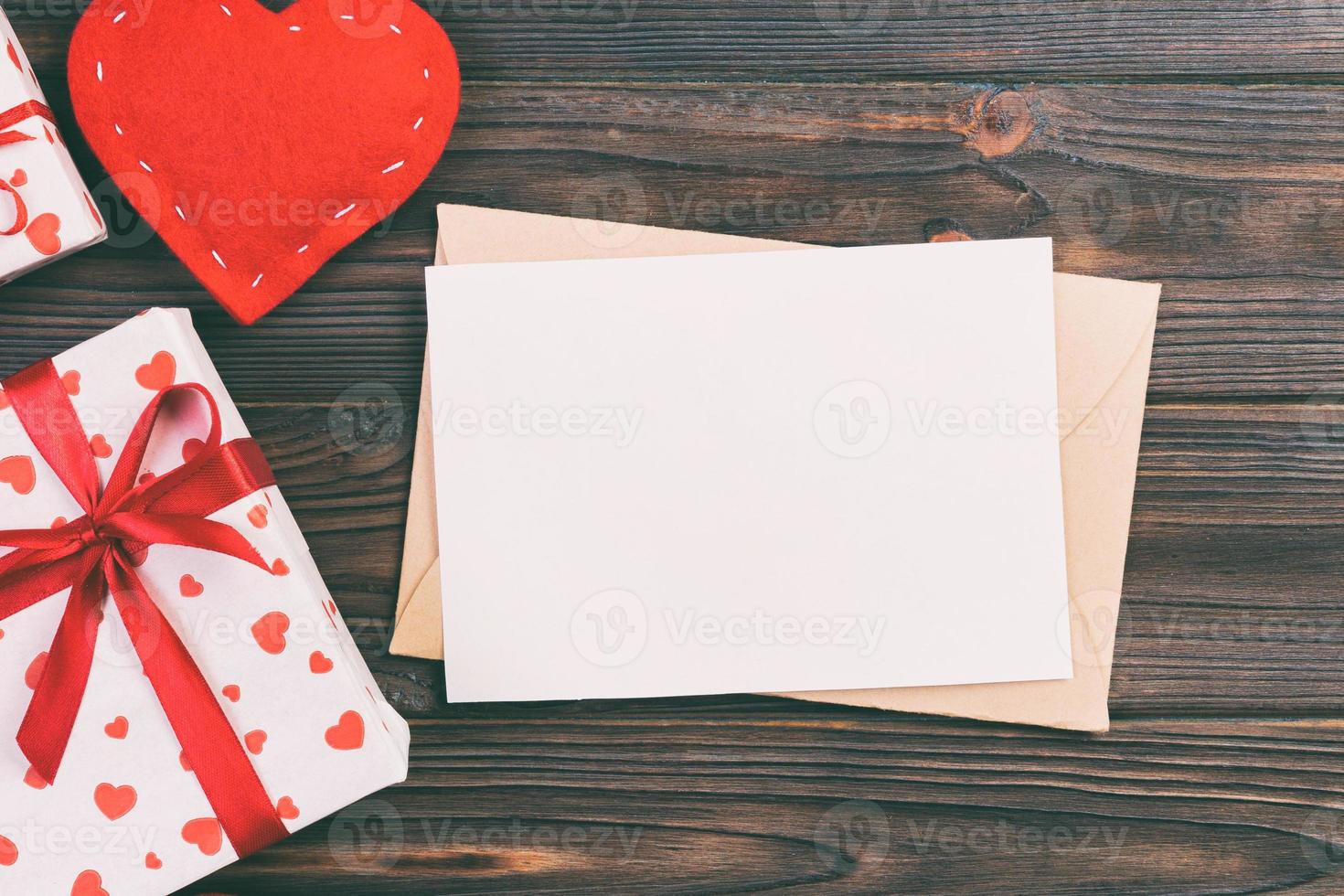Briefumschlag mit rotem Herzen und Geschenkbox auf dunklem Holzhintergrund. valentinstagkarte, liebes- oder hochzeitsgrußkonzept foto