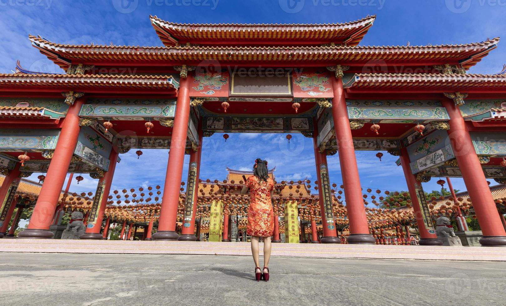 Rückansicht der asiatischen Frau im roten Cheongsam-Qipao-Kleid besucht den chinesischen buddhistischen Tempel während des neuen Mondjahres für das traditionelle Kulturkonzept. Das chinesische Wort bedeutet Segen für alle foto