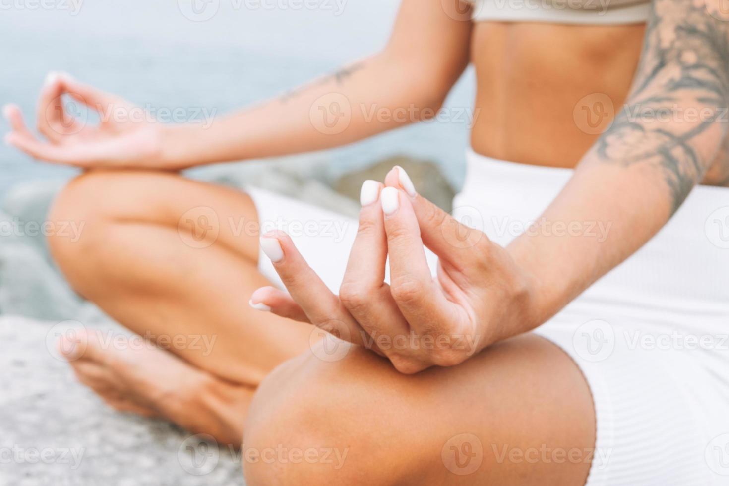 Erntefoto einer jungen, fitten, schönen Frau mit langen Haaren in weißer Sportkleidung, praktiziert Yoga und genießt das Leben am Meeresstrand, geistige und körperliche Gesundheit foto