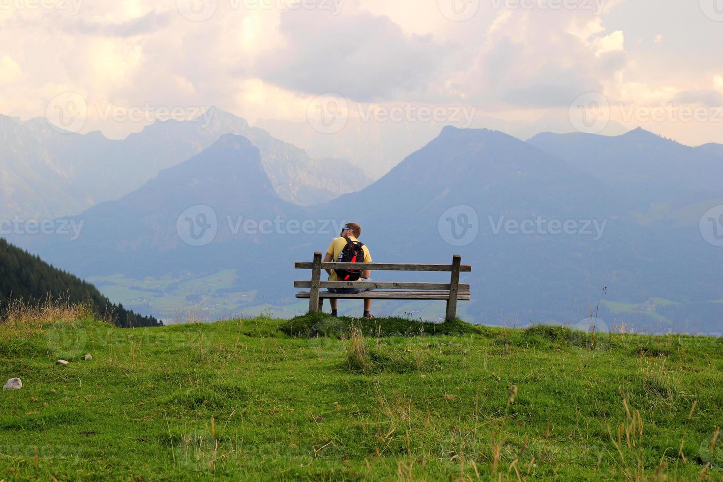 reise nach sankt-wolfgang, österreich. der junge mann sitzt auf einer bank mit blick auf die berge. foto