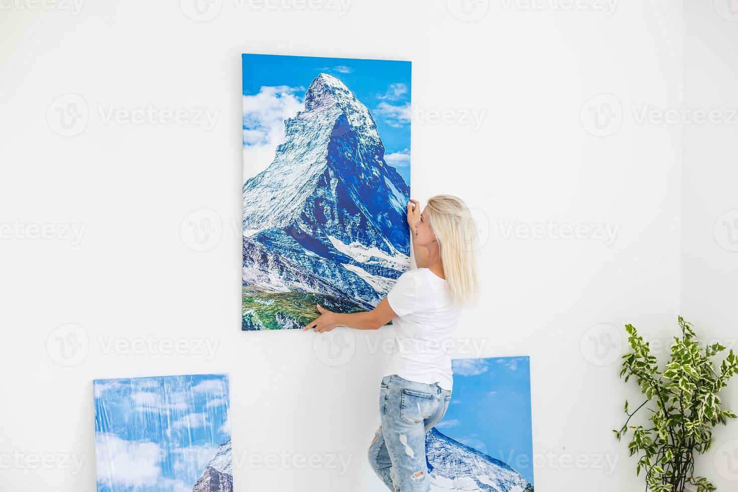 glückliche blonde frau, die zu hause ein großes bild an der wand hängt foto