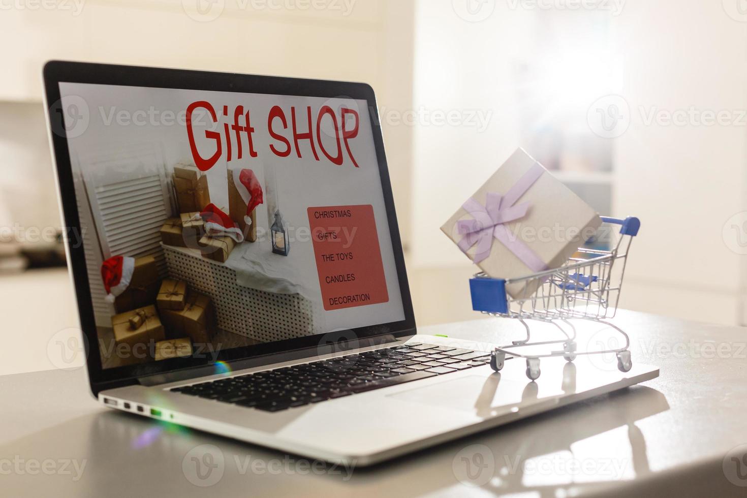 Einkaufswagen mit dekorativer Geschenkbox gegen Laptop mit Geschenken auf dem Bildschirm foto