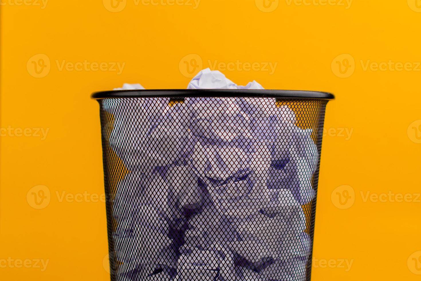 Weiße Papierfetzen im Mülleimer auf gelbem Hintergrund, Altpapierabfallkonzept foto