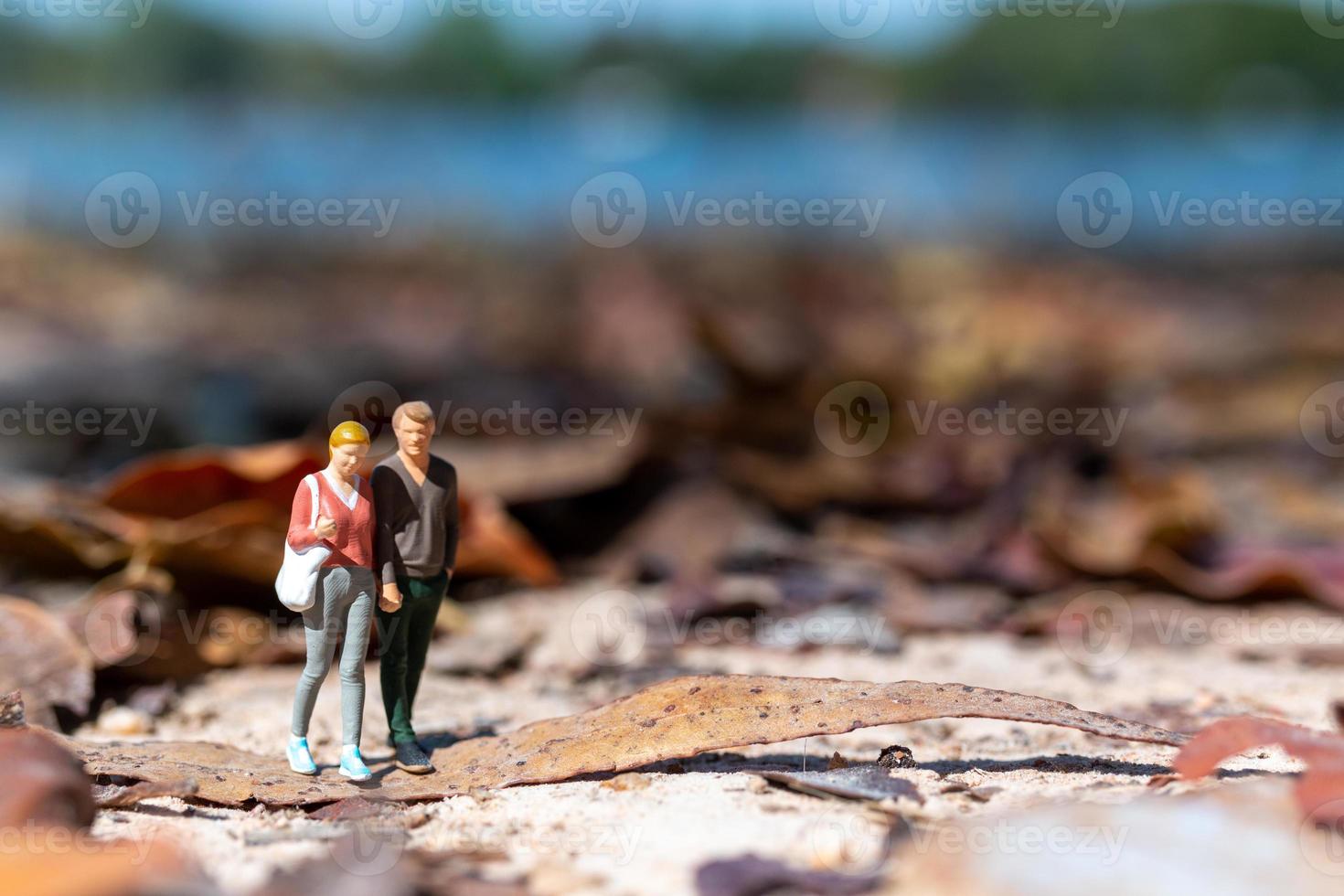 Miniaturmenschen, junge Liebende, die Händchen haltend im Herbst durch einen Park schlendern foto