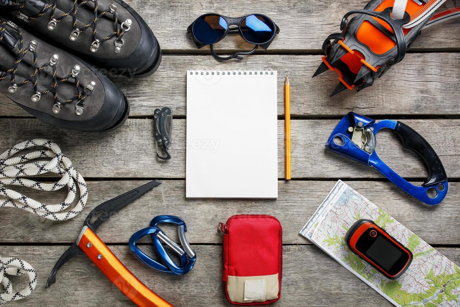 Draufsicht auf touristische Ausrüstung für eine Bergtour auf einem rustikalen hellen Holzboden mit einem Notizbuch und einem leeren Raum in der Mitte. foto