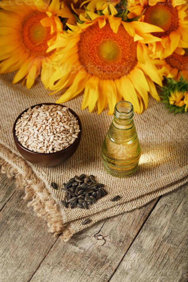 Sonnenblumenöl in einer Flasche mit Sonnenblumenkernen und Blumen auf Holzhintergrund. foto