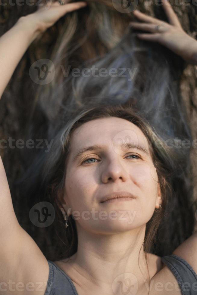 Nahaufnahme einer erwachsenen Frau, die auf Baumrinde liegt und Himmelsporträtbild betrachtet foto