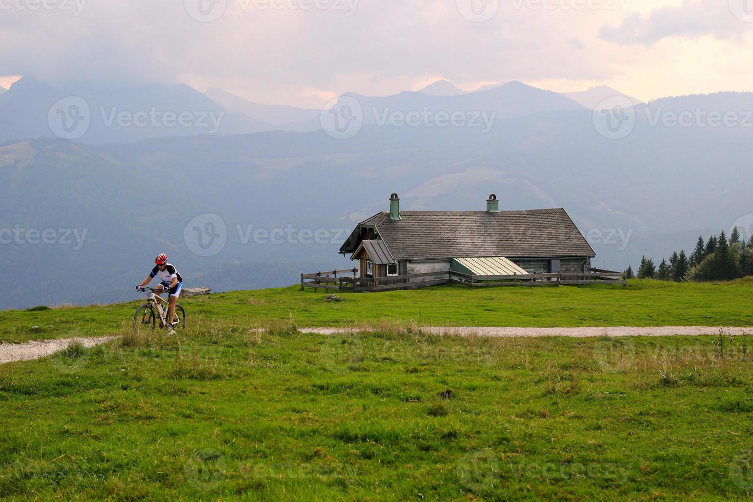 reise nach sankt-wolfgang, österreich. ein radfahrer auf der straße zwischen den feldern mit blick auf die berge und ein haus in den wolken. foto