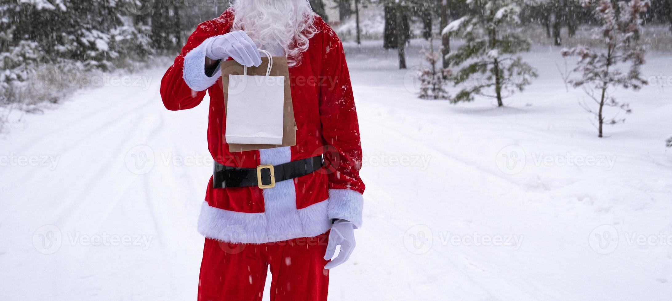 weihnachtsmann im freien im winter und schnee, der handpapiertüten mit handwerksgeschenk, lebensmittellieferung übergibt. Einkaufen, Verpackungsrecycling, Handarbeit, Lieferung für Weihnachten und Neujahr foto