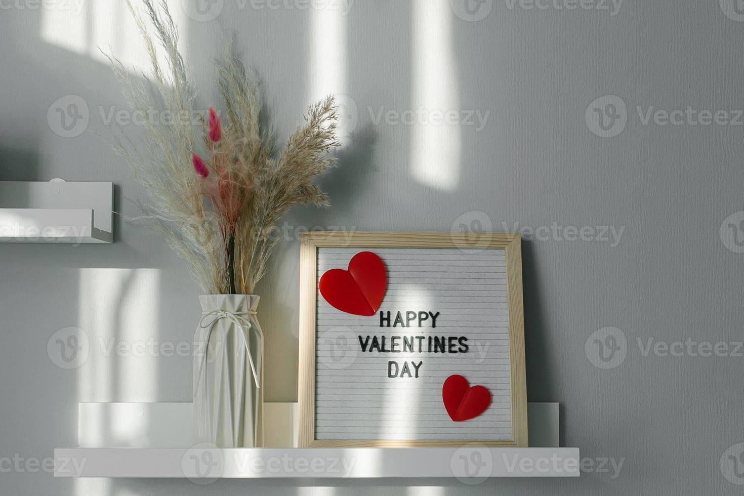 briefbrett mit text happy valentines day und vase mit trockenen blumen auf weißem regal im zimmer zu hause foto